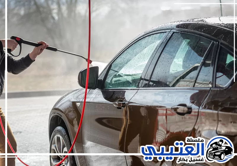 غسيل سيارة سوداء بالماء المضغوط لتنظيف الهيكل والزجاج وإزالة الأوساخ المتراكمة.
